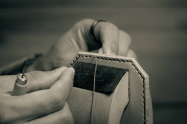 Sebzeli, bronzlaşmış deriyi elle dikiyorum. Deri ve el işi aletleri. Monoton ve yüzeysel alan derinliği.