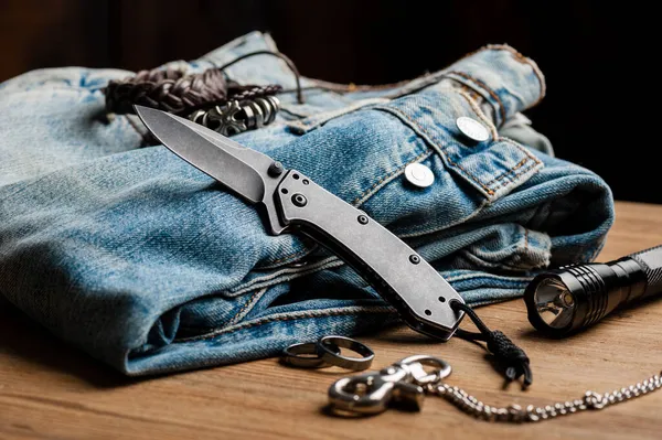 ナイフとジーンズを折る ブレードとハンドルにブラックウォッシュ仕上げのステンレス製ポケットナイフを閉じます ロイヤリティフリーのストック写真