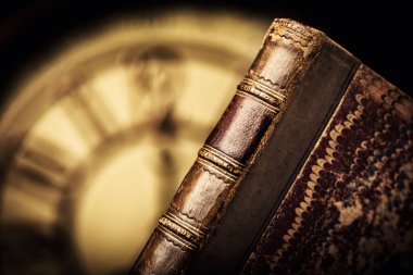 Arka planda saat yüzü olan antika deri ciltli bir kitap..