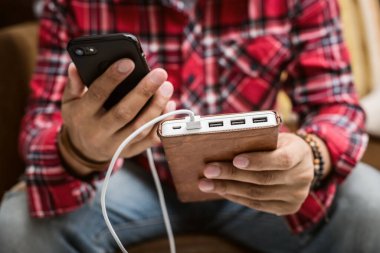 Kırmızı gömlekli adam akıllı telefonu beyaz güç bankasıyla şarj ediyor.. 