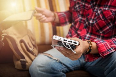 Kırmızı gömlekli adam akıllı telefonu beyaz güç bankasıyla şarj ediyor.. 