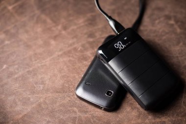 Siyah güç bankası USB kablosuna bağlı. Elektrik bankasıyla elektronik cihazı şarj ediyorum. Güç bankası görüntüsüne odaklanmış sığ alan derinliği.