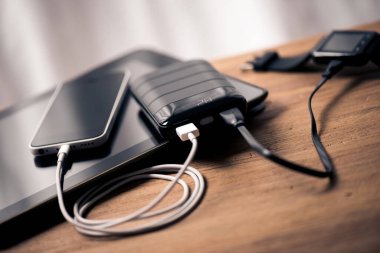 Siyah güç bankası USB kablosuna bağlı. Akıllı telefonu güç bankasıyla şarj ediyor. Güç bankası görüntüsüne odaklanmış sığ alan derinliği.