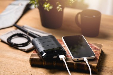 Siyah güç bankası USB kablosuna bağlı. Akıllı telefonu güç bankasıyla şarj ediyor. Güç bankası görüntüsüne odaklanmış sığ alan derinliği.
