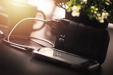 Siyah güç bankası USB kablosuna bağlı. Akıllı telefonu güç bankasıyla şarj ediyor. Güç bankası görüntüsüne odaklanmış sığ alan derinliği.