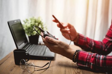 Siyah güç bankası USB kablosuna bağlı. Akıllı telefonu güç bankasıyla şarj ediyor. Güç bankası görüntüsüne odaklanmış sığ alan derinliği.