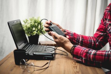 Siyah güç bankası USB kablosuna bağlı. Akıllı telefonu güç bankasıyla şarj ediyor. Güç bankası görüntüsüne odaklanmış sığ alan derinliği.