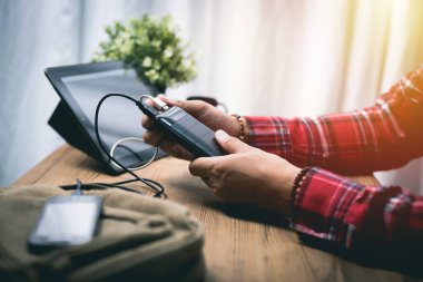 Siyah güç bankası USB kablosuna bağlı. Akıllı telefonu güç bankasıyla şarj ediyor. Güç bankası görüntüsüne odaklanmış sığ alan derinliği.