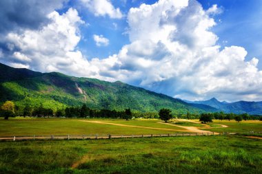 Bulutlu bir günde arka planda dağ sırasıyla güzel bir kır manzarası..