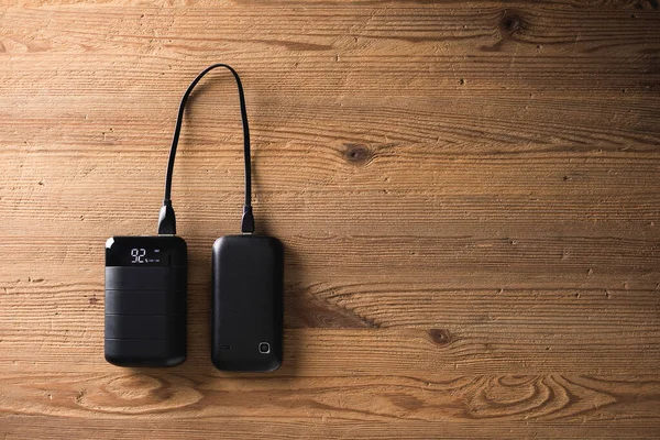 Black power bank connected with USB cable. Charging smartphone with power bank. Shallow depth of field focused on power bank display.