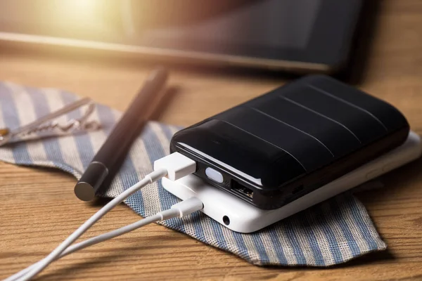 Black power bank connected with USB cable. Charging smartphone with power bank. Shallow depth of field focused on power bank display.