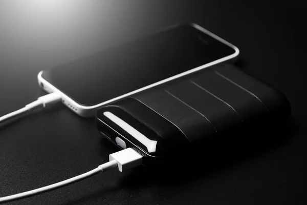 Black power bank connected with USB cable. Charging smartphone with power bank. Shallow depth of field focused on power bank display.
