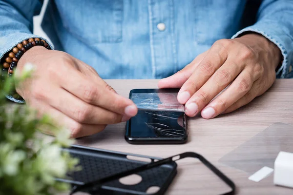 The man replacing the broken tempered glass screen protector for smartphone.