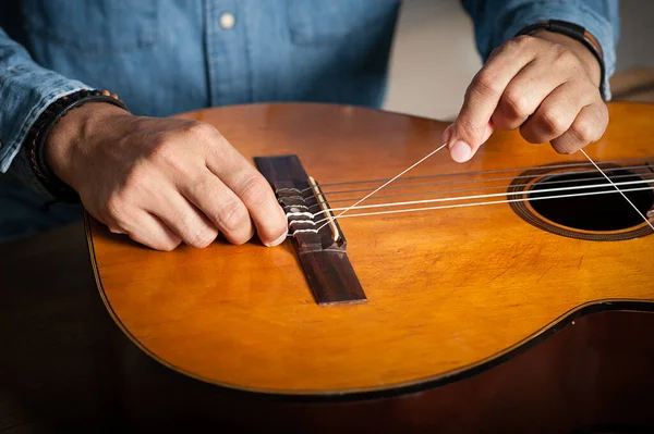 closeup man\'s hand changing strings on his old acoustic guitar.