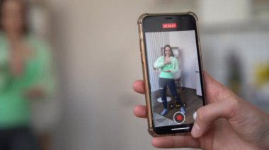 Kız akıllı telefonun önünde eğleniyor, dans ediyor. Moda dansları yapan şık elbiseli bir kız. Uygulama kullanarak dans videosu oluşturuluyor.