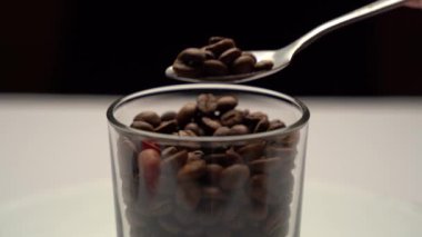 Kokulu kahve çekirdekli bardağa yakın çekim. Çay kaşığıyla erkeklerin eli birkaç kahve çekirdeği topluyor.