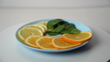 Olgun narenciye dilimleri ve nane yaprakları bir tabakta dönüyor. Meyveler bir tabakta 360 derece döner. Limonata yapmak için gerekli malzemeler