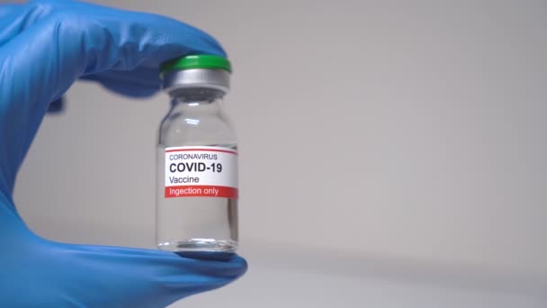 一只手戴着蓝色的医疗手套 手里拿着一瓶玻璃杯水 预防Covid 19的疫苗 疫苗对人类健康的好处 图库视频片段