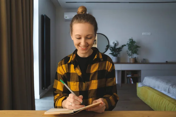 Happy girl at the desk, writing in the notebook 스톡 이미지