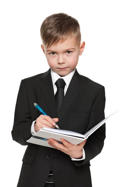 Ernster kleiner Junge im schwarzen Anzug mit Notizbuch — Stockfoto