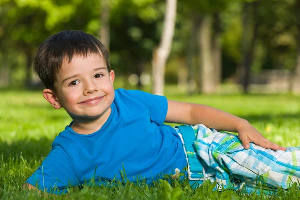 Rapaz bonito em camisa azul na grama . — Fotografia de Stock