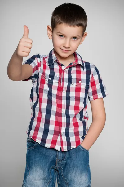 Jonge jongen houdt zijn duim omhoog op de grijze achtergrond — Stockfoto