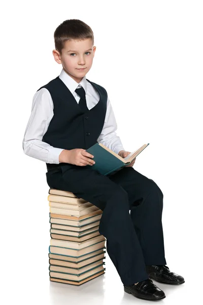 Niño con un libro está sentado en la pila de libros — Foto de Stock