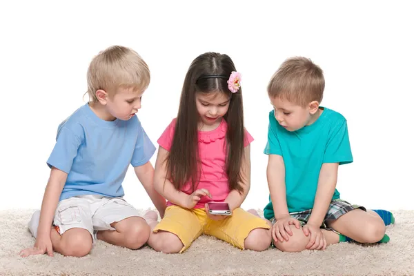 Crianças com um gadget no tapete branco — Fotografia de Stock