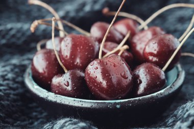 Koyu mavi örülü bir battaniye üzerinde olgun kırmızı kirazlarla dolu bir kase..