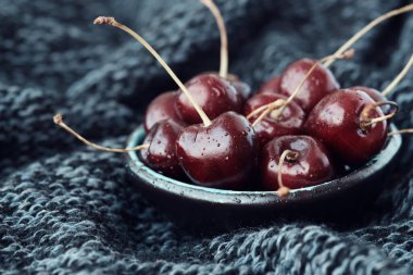 Koyu mavi örülü bir battaniye üzerinde olgun kırmızı kirazlarla dolu bir kase..