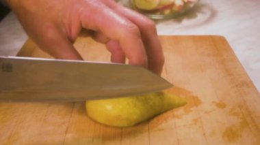 Kadınların elleri mutfak tahtasındaki bıçakla armudu kesiyor..