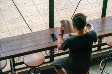 Asyalı adam kitap okuyor ve sabahları kahve içiyor.