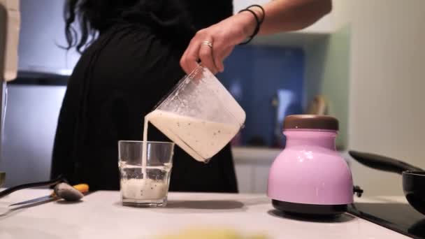 Närbild på en kvinna häller hälsosam banan smoothie i ett glas i köket. — Stockvideo