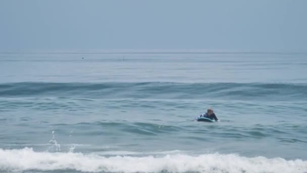 Surfer na desce surfingowej unoszący się w błękitnym morzu czekając na fale surfingowe — Wideo stockowe