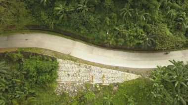 Arka planda dağlar olan bir yolda motosiklet süren bir adam. Ormandaki bir dağ yolunda Moped süren genç bir adamın hava görüntüsü.