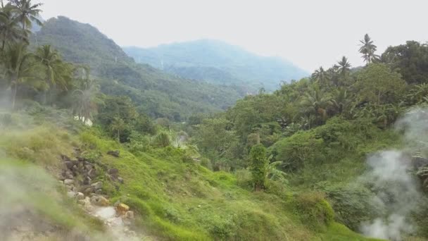 Вид с воздуха Пар выходит из земли в зеленом лесу, вокруг горы и реки — стоковое видео