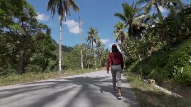 Молода азіатка йде по дорозі, дивиться на природу в джунглях лісу, гора террейн, навколо пальмових дерев — стокове відео