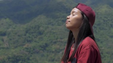 Genç bir Asyalı kadın Lotus pozisyonunda bir dağda oturuyor, Ormanı gören bir manzarayla doğada meditasyon yapıyor.