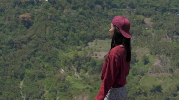 Asiatisk ung kvinna tittar på berget och ser sig omkring i Asien, reser genom djungeln bland palmer i soligt väder — Stockvideo