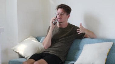 Genç modern adam kanepede otururken telefonla iletişim kuruyor. Mutlu adam, içerideki telefonu ara.