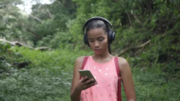 Νεαρό χαρούμενο ενεργό σπορ κορίτσι περπάτημα με ακουστικά κινητό τηλέφωνο απολαμβάνοντας ακούγοντας μουσική, τζόκινγκ σε εξωτερικούς χώρους στο αστικό πάρκο της πόλης ή δάσος φόντο ασιατική γυναίκα κάνει γυμναστική ακουστικά — Αρχείο Βίντεο