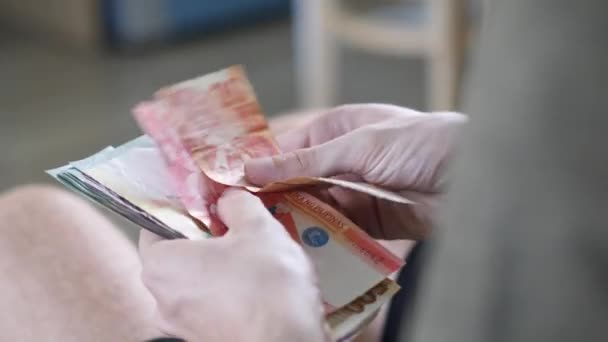 Las manos de los hombres cuentan en efectivo pesos filipinos y otras monedas en casa en una habitación luminosa — Vídeo de stock