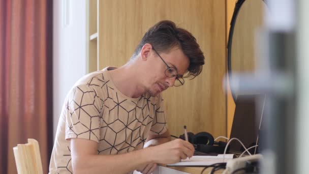 Молода європейська людина з думкою пише з ручкою в записнику, приписує свої плани, студії та студії вдома — стокове відео