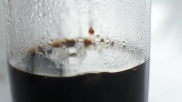 Masanın üzerinde duran şeffaf bir camın yakın çekimi, damlatan kahve damlaları — Stok video