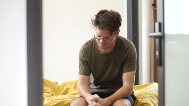 Mladý Evropan je nervózní, když sedí doma na posteli ve světlém pokoji. — Stock video