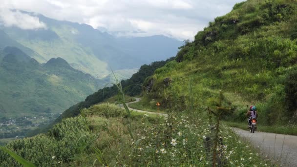 Motos com jovens estão andando ao longo da estrada, nas montanhas ao redor da floresta, uma vista de uma bela rocha e campos de arroz — Vídeo de Stock