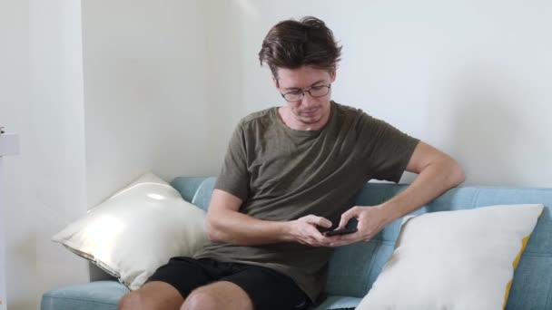 Frustrated young man looking at smartphone screen, feeling disappointed with received bad news message. Stressed millennial guy reading sms, frustrated by annoyed bank loan notification indoors. — Stock Video