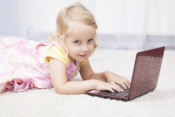 Little girl lying on floor working with a laptop — Stock Photo, Image