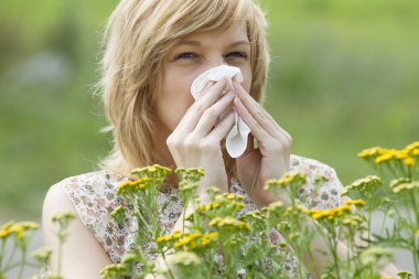 Woman blowing nose into tissue outdoors
