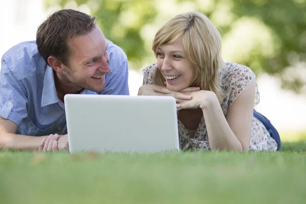 Paar liegt mit Laptop im Park auf Gras — Stockfoto